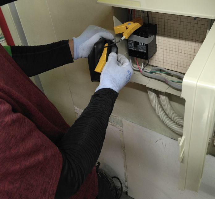 分電盤の電流をクランプメーターで測る作業員の手元